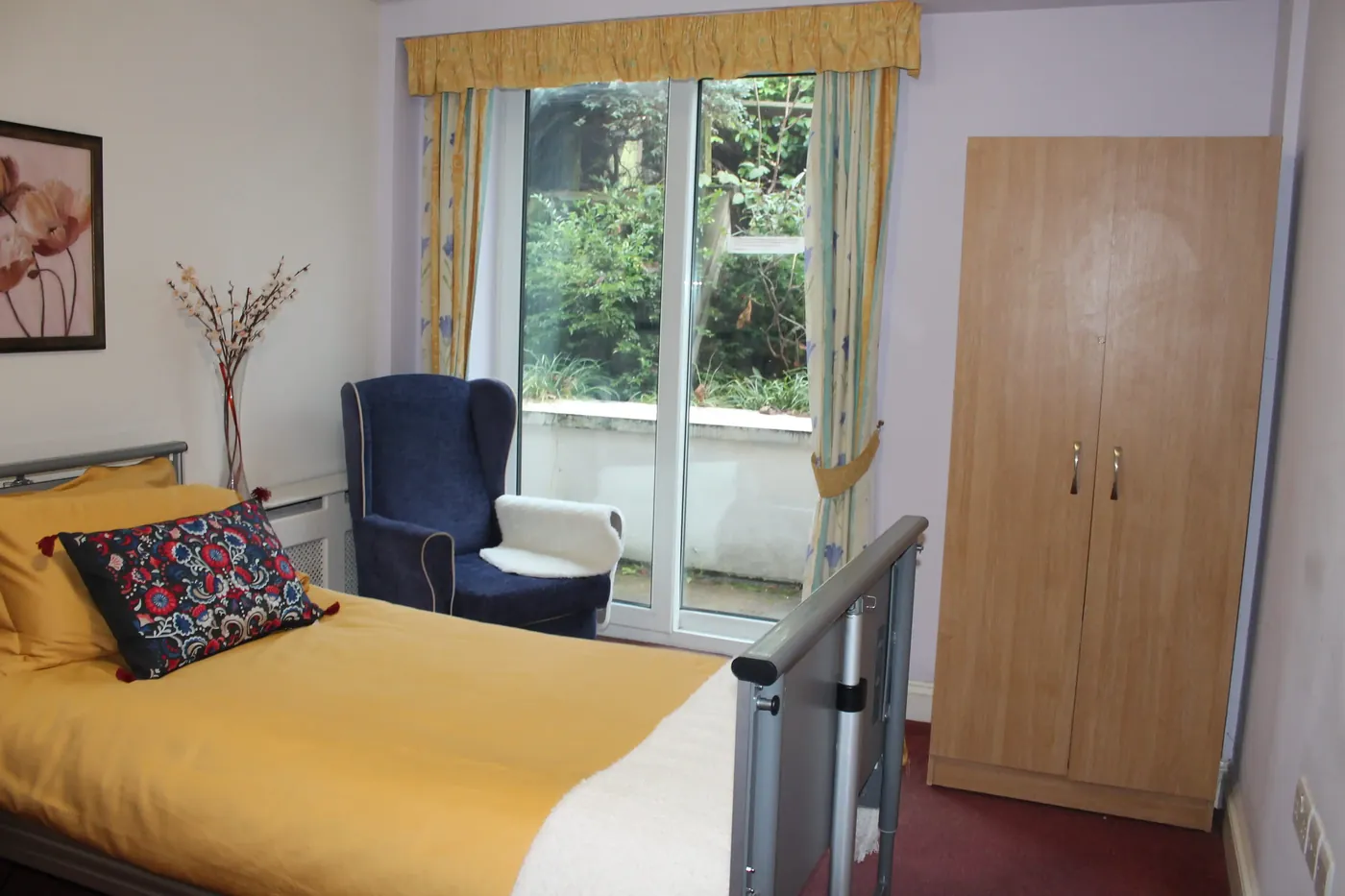 Bedroom with an armchair by glass doors onto the garden at Parkview Nursing Home